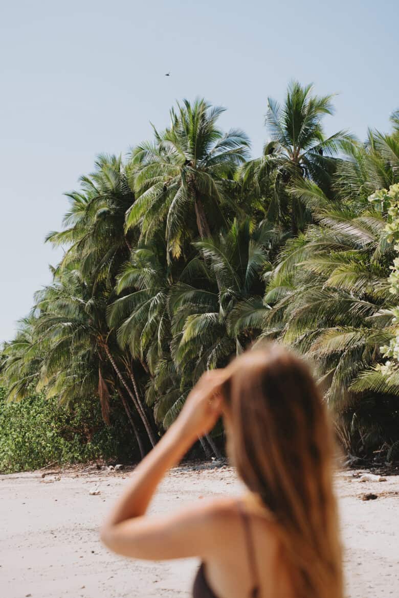 A woman in a bikini standing on a beach in Montezuma, Costa Rica, with palm trees in the background.