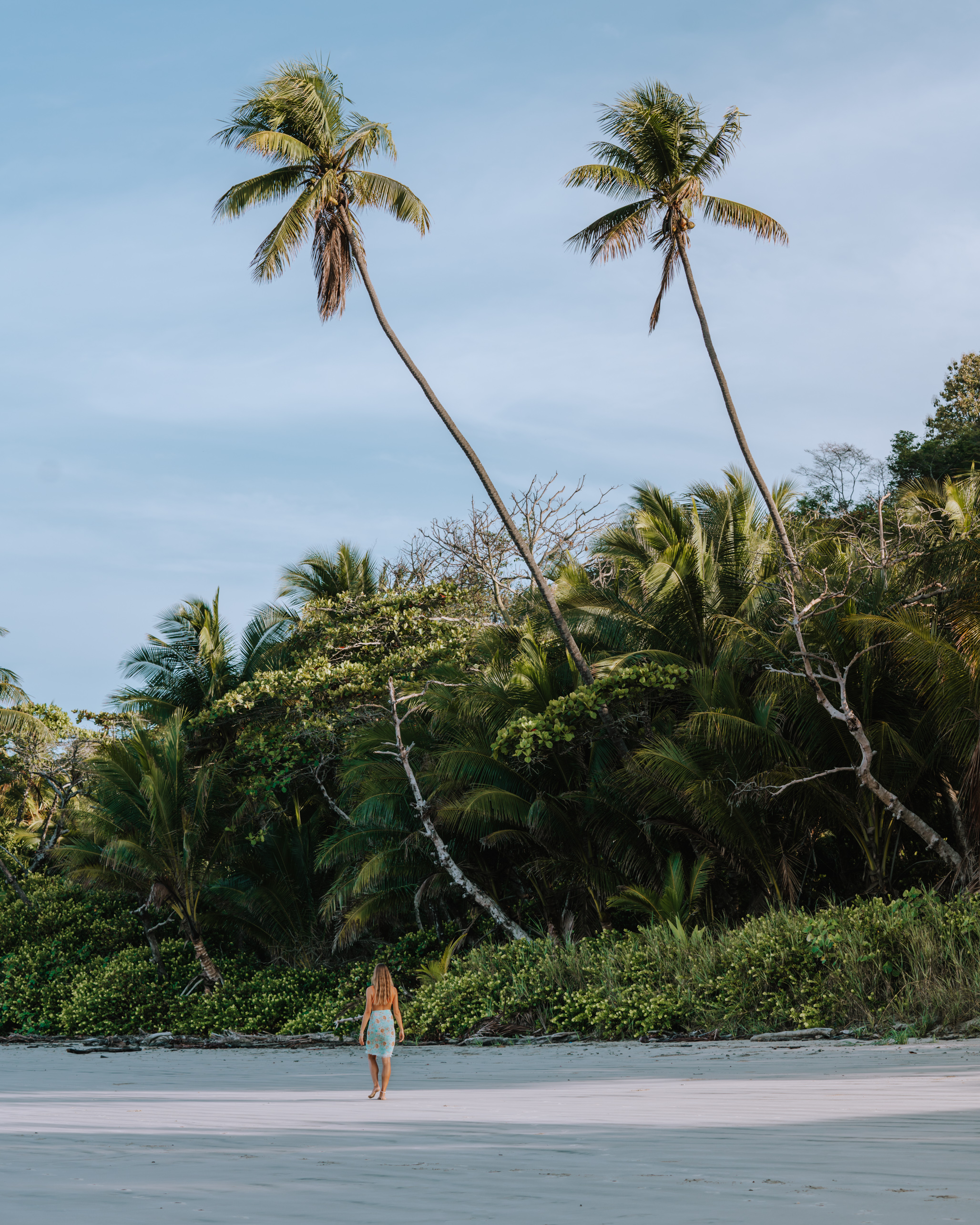 A woman walking on a Santa Teresa beach with palm trees in the background.